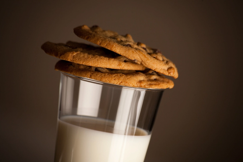 Three chocolate chip cookies stacked on a glass of milk