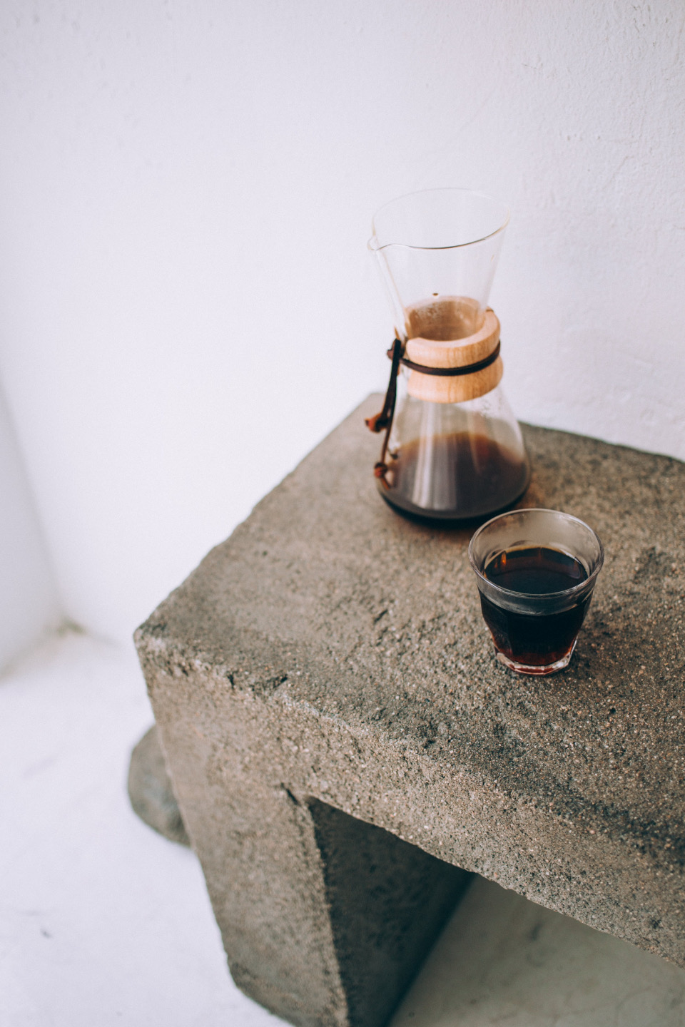 A glass coffee carafe and a cup on a concrete ledge in soft light