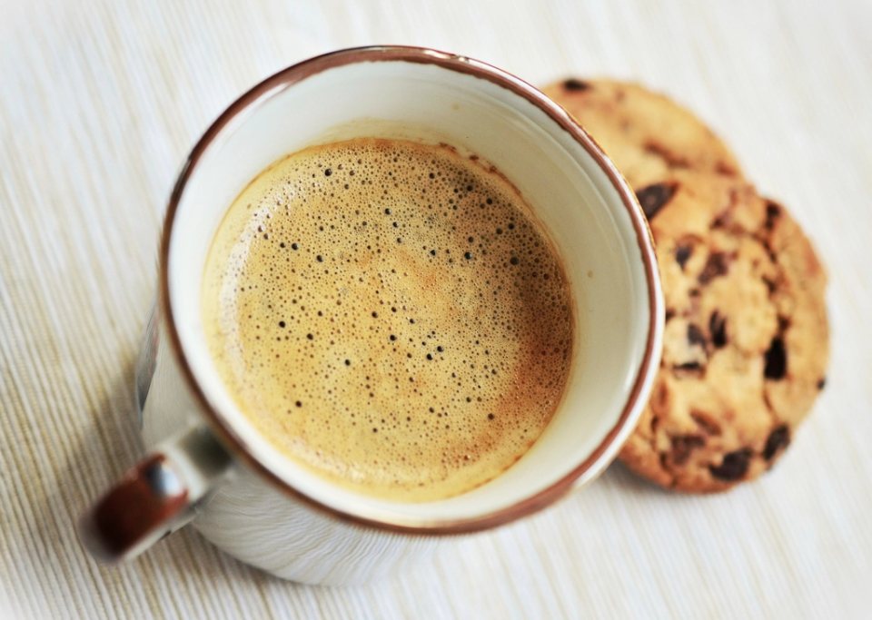 A fresh coffee with crema beside chocolate chip cookies