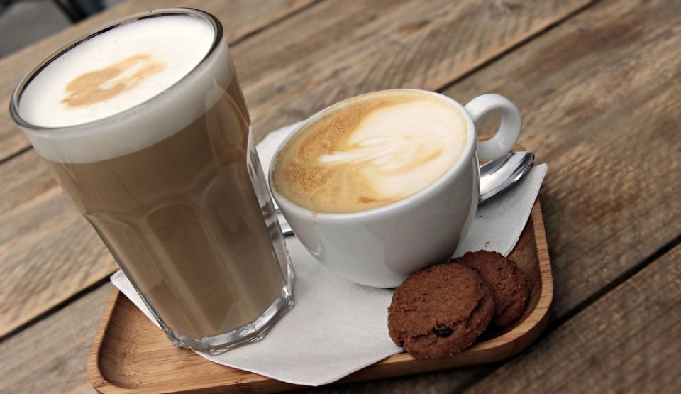 A latte and a cappuccino with chocolate cookies on a wooden tray