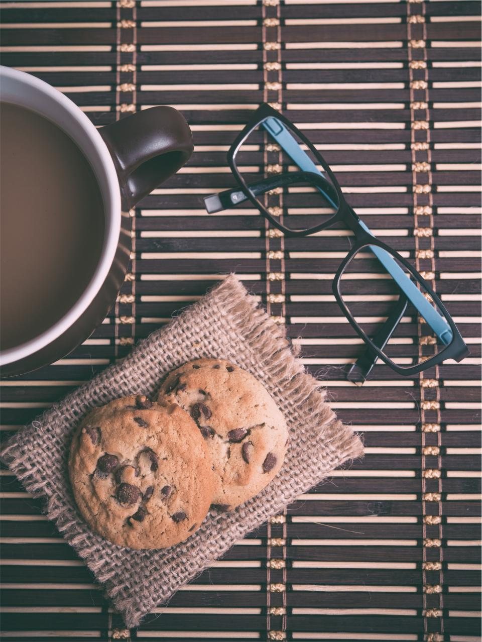 Chocolate chip cookies on a linen napkin beside a coffee and reading glasses